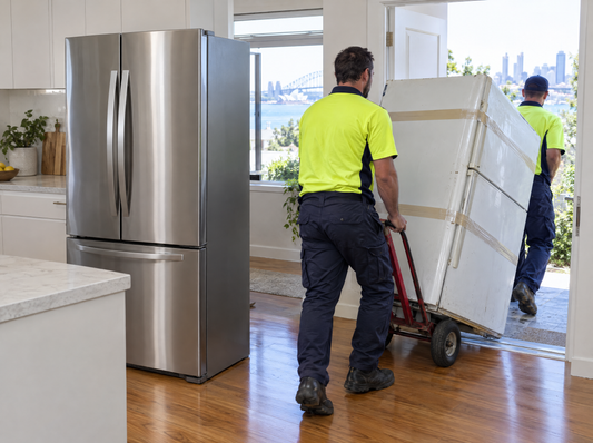 Removal workers wheeling an old taped-shut fridge out of a Sydney kitchen after a new stainless-steel fridge was installed